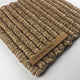 A richly textured honey-toned mat crafted from thick, braided abaca fibers with a subtle wooden label at one corner.