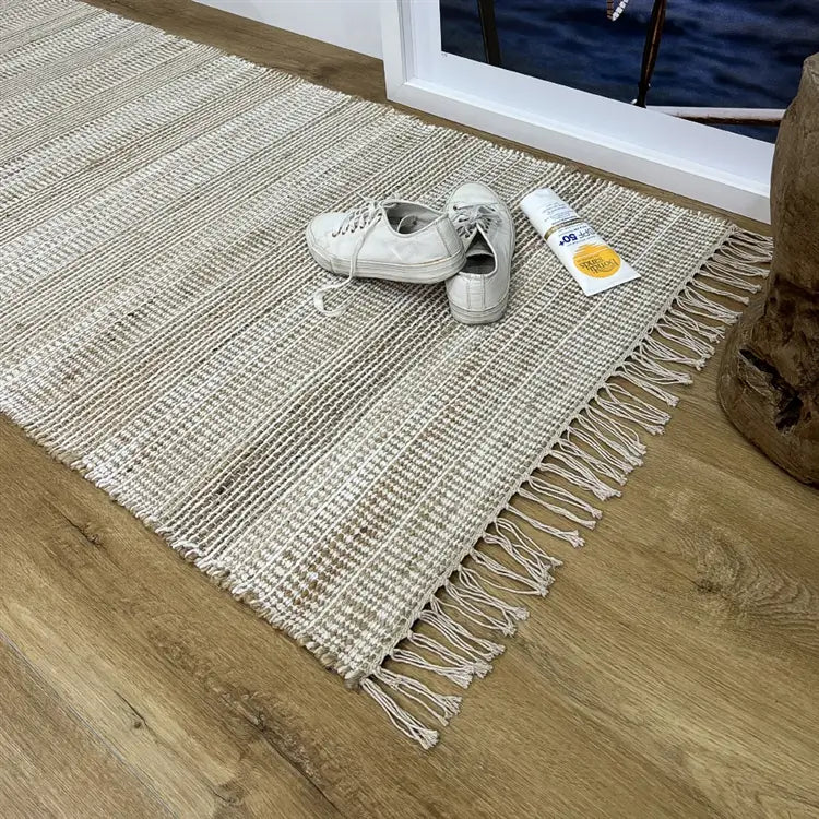 A white natural fibre runner on timber flooring, styled with white sneakers and sunscreen beside a framed artwork in a modern interior.