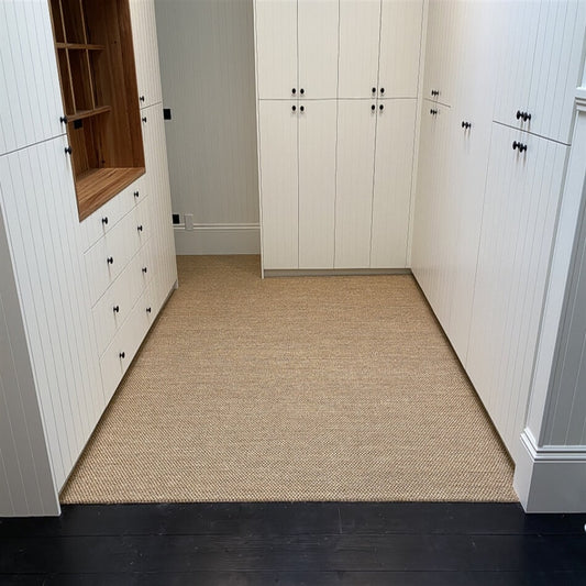 Spacious walk-in closet with white paneled cabinets, black handles, and a rustic sisal rug enhancing the refined interior.