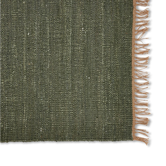 Moss green jute rug with a tan fringe edge, showcasing rich texture and refined craftsmanship on natural fibre flooring.