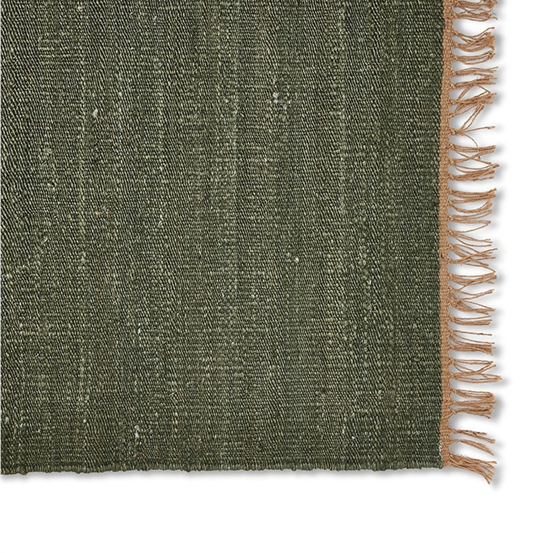 Moss green jute rug with a tan fringe edge, showcasing rich texture and refined craftsmanship on natural fibre flooring.