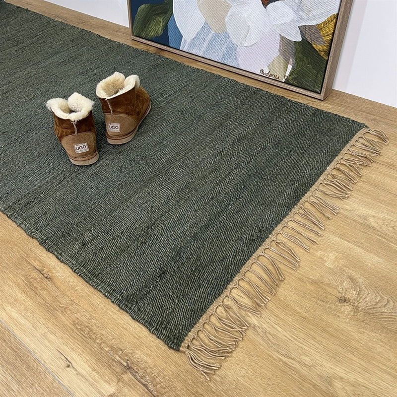 Brown shearling boots rest on a textured moss jute runner, set beside a floral wood painting in a thoughtfully styled interior.