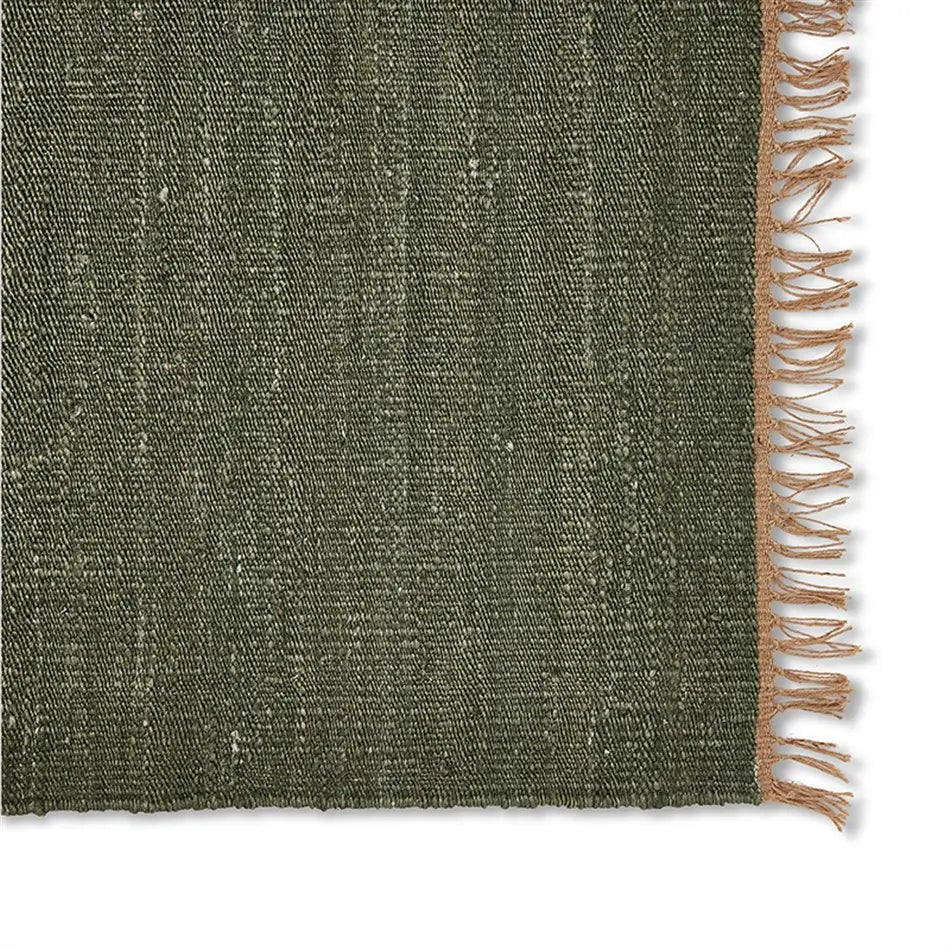 Close-up of an olive green jute rug with beige fringe, highlighting the rich texture and natural fibers on a white background.