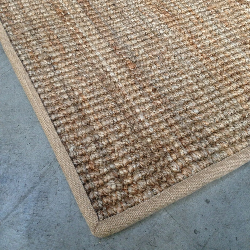 Natural fibre rug with refined hessian border rests on smooth concrete flooring, highlighting artisan quality and enduring style.