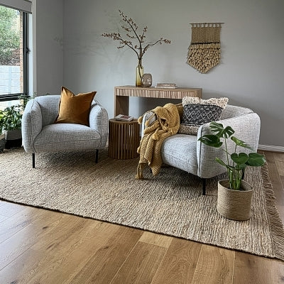 A styled living room features two grey armchairs and a premium natural fibre rug, with plants and curated decorative accents.