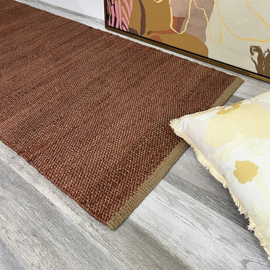 Ochre jute runner on grey wood floor, paired with a white floral pillow and abstract art in a refined, styled interior.
