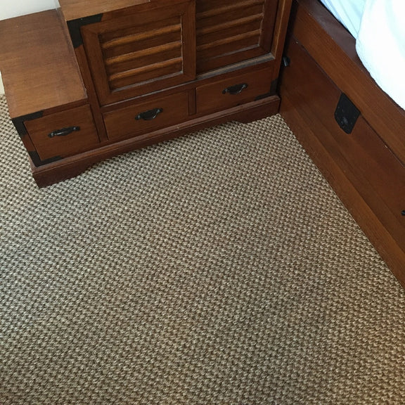 A sturdy wooden bed and matching furniture sit on richly textured rustic quartz sisal carpet in a thoughtfully styled bedroom corner.