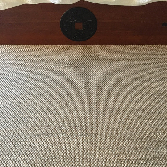 A textured sisal rug with rich natural fibres lies before a wooden bed accented by a central round carved wood ornament.