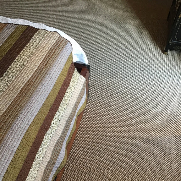 A striped quilted bed rests on elegant rustic quartz sisal flooring, with a book partially tucked beneath the bedspread.