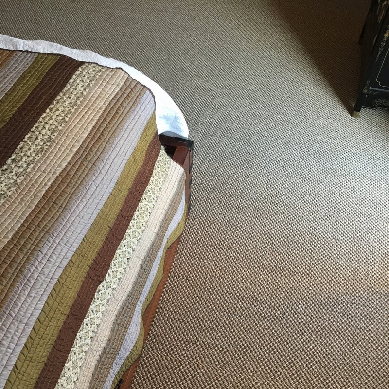A striped quilted bed rests on elegant rustic quartz sisal flooring, with a book partially tucked beneath the bedspread.
