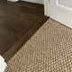 Rich dark hardwood flooring seamlessly transitions to a textured sisal rug in soft river rock tones, styled beside a white doorway.