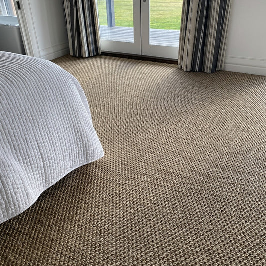 Elegant sisal flooring with a textured river rock weave in a serene bedroom, paired with a white bedspread and striped curtains.