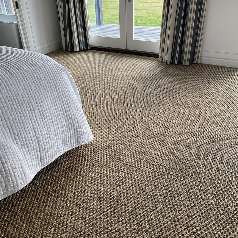 Elegant sisal flooring with a textured river rock weave in a serene bedroom, paired with a white bedspread and striped curtains.