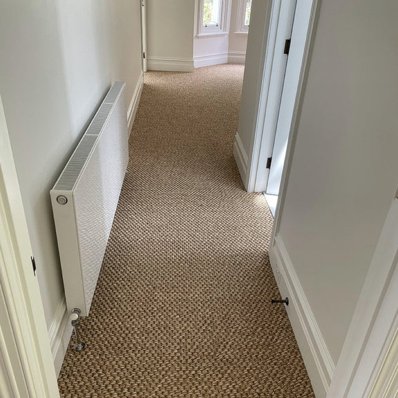 Bright hallway featuring textured rustic river rock sisal flooring, white radiator on the left, and an open door to the right.