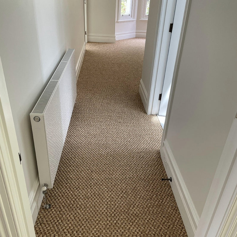 Bright hallway featuring textured rustic river rock sisal flooring, white radiator on the left, and an open door to the right.