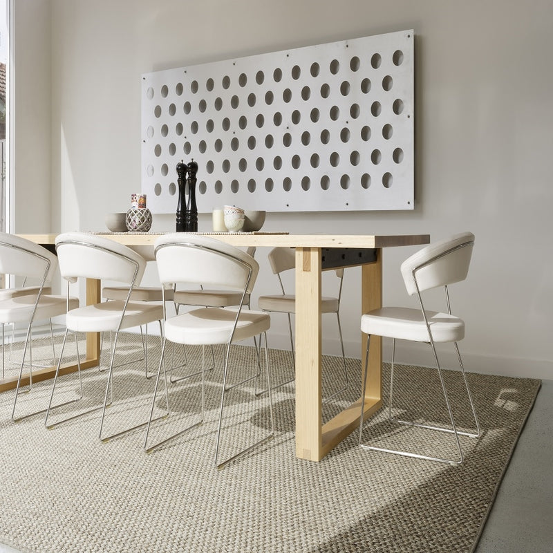 Contemporary dining space with a wooden table, six white chairs, and a handwoven rustic sisal rug anchoring the setting.