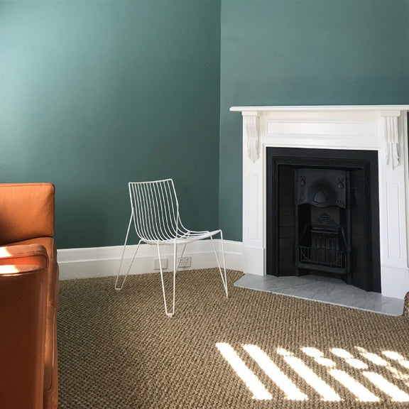 Sunlight fills a refined room with a green wall, white fireplace, modern seating and a heavy sisal rug showcasing natural texture.