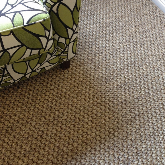 A green and white armchair sits atop textured, natural sisal carpet, bathed in gentle side light within a serene styled space.