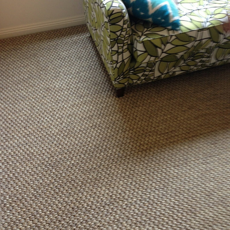 A green leaf-patterned sofa sits atop textured, natural sisal flooring, accented by a blue and white pillow in a styled interior.