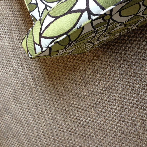A green and white cushion sits on a textured sisal rug with a river rock pattern, styled in an inviting, natural interior setting.