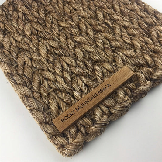 A thick abaca rug in a warm, natural weave showcases a subtle wooden label, highlighting artisanal quality and sustainable elegance.