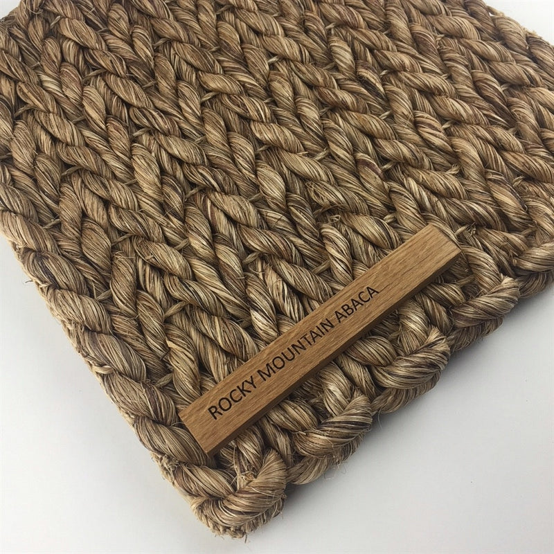 A thick abaca rug in a warm, natural weave showcases a subtle wooden label, highlighting artisanal quality and sustainable elegance.