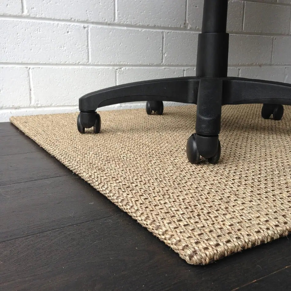 A finely woven sisal chair pad in Autumn Slate rests beneath an office chair, enhancing and protecting a dark timber floor.