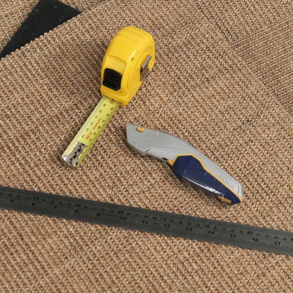 A tape measure, utility knife, and metal ruler rest on textured natural sisal tiles, highlighting quality and artisanal detail.