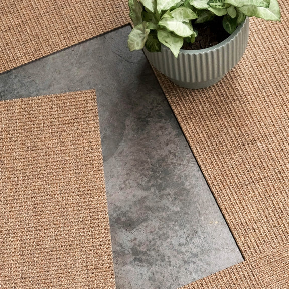 A lush potted plant rests atop textured natural sisal tiles, accented by a refined gray stone detail in a bright, styled interior.