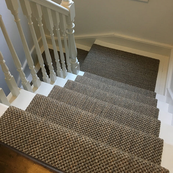Sunlit staircase with plush white railings and a handwoven sisal runner in fine rustic slate, elevating a refined home interior.