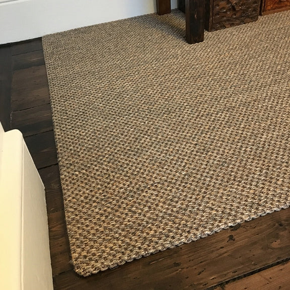 A rustic slate sisal carpet sits atop dark timber flooring, complemented by white walls and refined wood furniture in a styled interior.