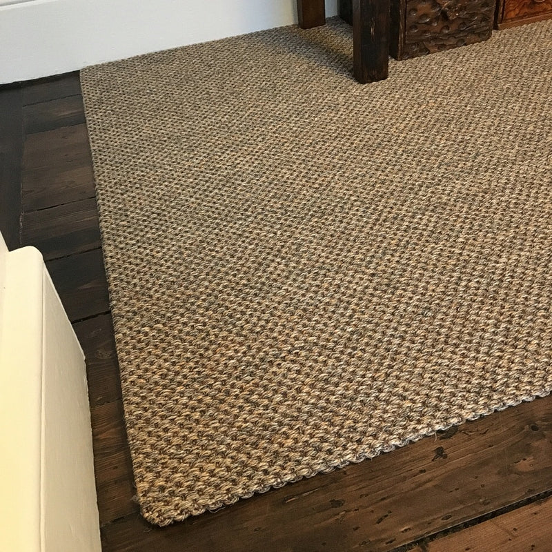 A rustic slate sisal carpet sits atop dark timber flooring, complemented by white walls and refined wood furniture in a styled interior.