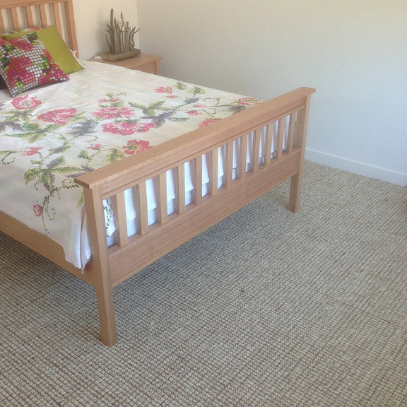Minimal bedroom with a wooden bed, floral bedding, and a green pillow atop a natural wool and jute rug on timber floors.