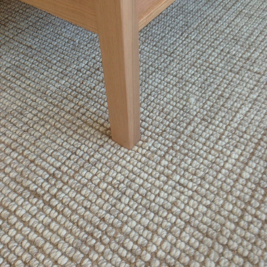 Elegant wooden furniture leg resting on a textured wool and jute floorcovering in a thoughtfully styled, modern interior.