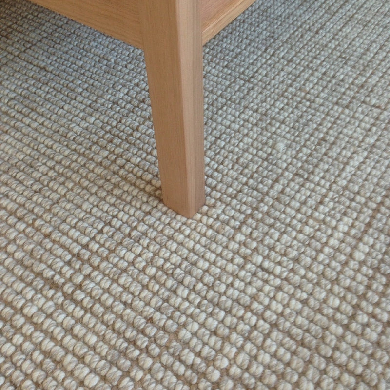 Elegant wooden furniture leg resting on a textured wool and jute floorcovering in a thoughtfully styled, modern interior.