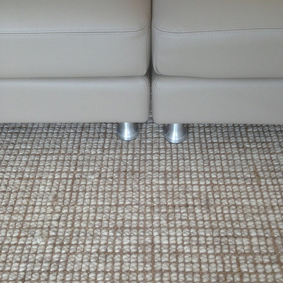 Beige leather sofa with sleek metal legs on a wool and jute blend rug, styled in an elegant, light-filled living room.