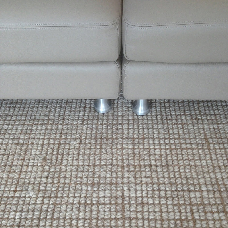 Beige leather sofa with sleek metal legs on a wool and jute blend rug, styled in an elegant, light-filled living room.