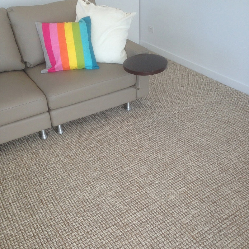 A light-toned sofa with white and rainbow pillows, next to a round side table on a wool-jute rug in a refined living space.