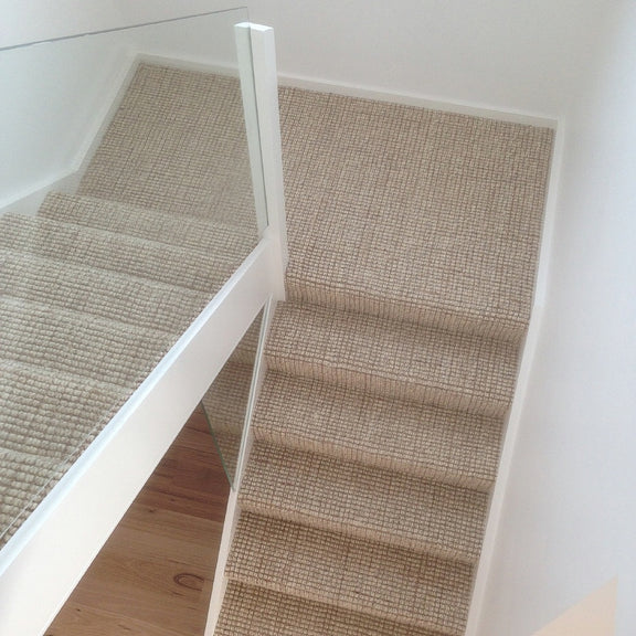 Staircase with beige wool and jute carpet, glass balustrade, and white walls, styled in an elegant contemporary home.