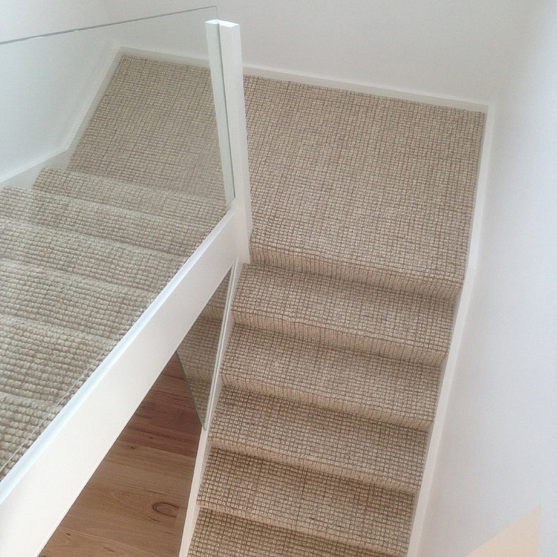 Staircase with beige wool and jute carpet, glass balustrade, and white walls, styled in an elegant contemporary home.
