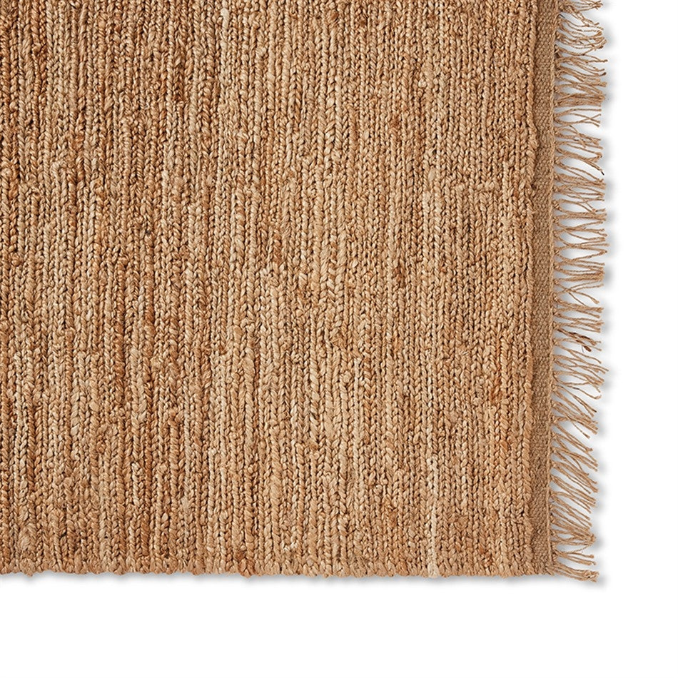 Elegant close-up of a handwoven jute rug with natural fringe, highlighting rich texture and artisanal craftsmanship on white.
