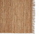 Detailed view of a handwoven tan jute rug with textured weave and delicate fringe, styled in a contemporary urban interior.