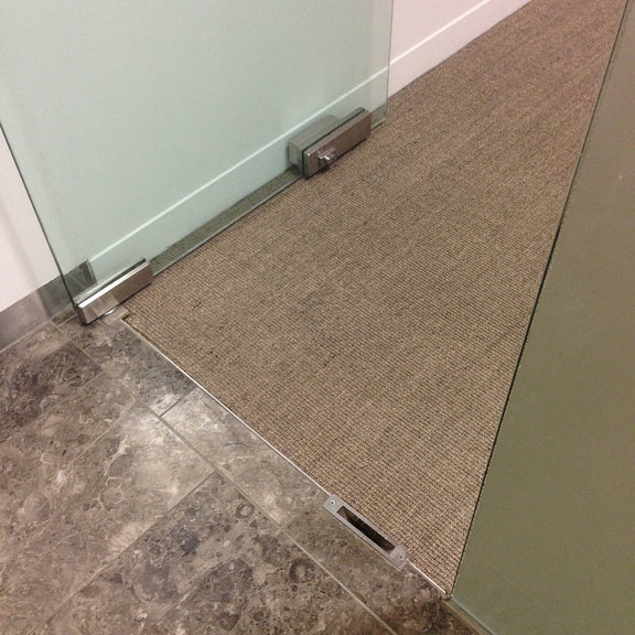 A sleek glass door seamlessly aligns with a clear wall, adjacent to tile flooring and a fine ribbed granite-hued sisal rug.
