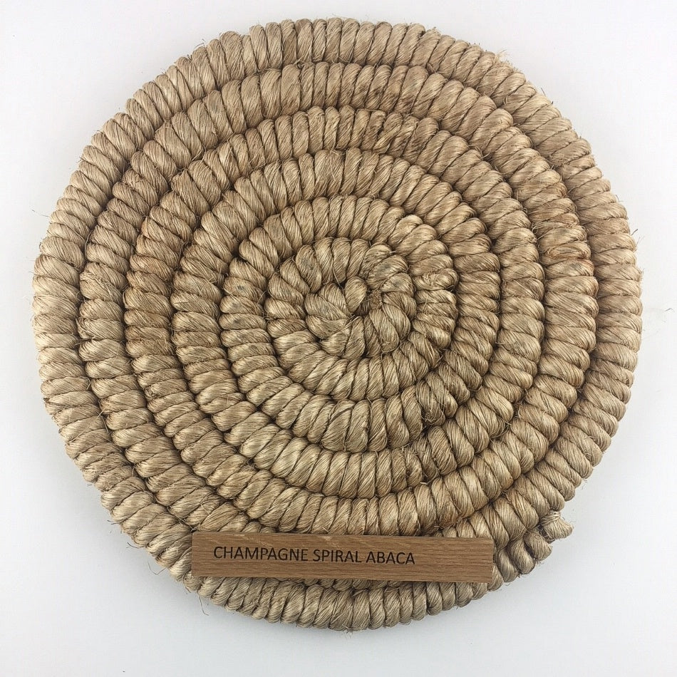 A round, coiled spiral weave rug in champagne-hued abaca, showcasing artisanal craftsmanship and refined natural texture.