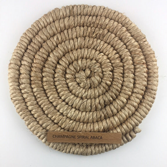 A round, coiled spiral weave rug in champagne-hued abaca, showcasing artisanal craftsmanship and refined natural texture.