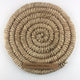 A round, coiled spiral weave rug in champagne-hued abaca, showcasing artisanal craftsmanship and refined natural texture.