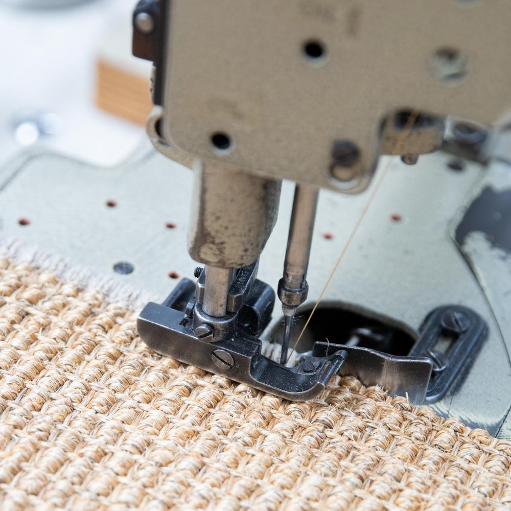 Sewing machine carefully stitching durable natural fibre rug with beige thread, highlighting expert craftsmanship and quality.