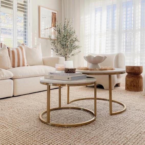 A sunlit living room featuring a beige sofa, layered natural fibre rug, round gold tables and soft neutral decor.