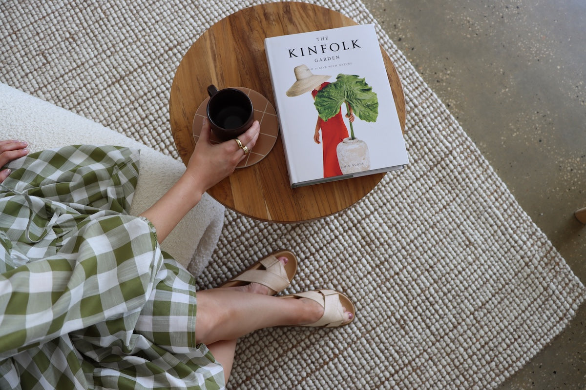 A woman in a green plaid dress enjoys coffee beside a round table, set on beautifully crafted natural fibre flooring.