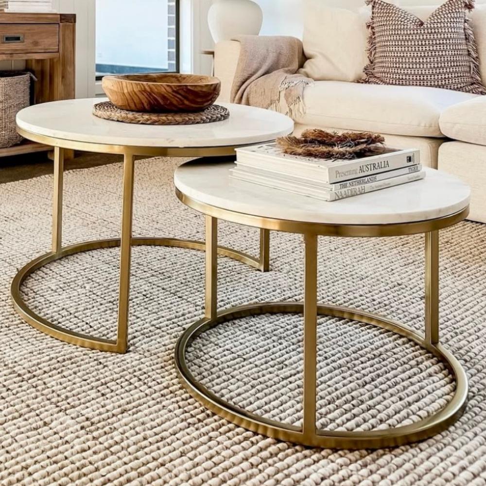 Two round coffee tables with gold frames rest on a premium natural fibre rug in a softly lit, elegantly styled living room.